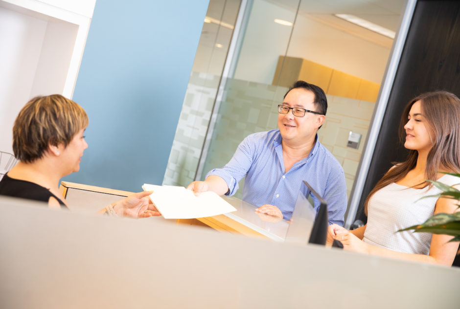 Attorney Dennis Chong handing documents to a woman at a desk.